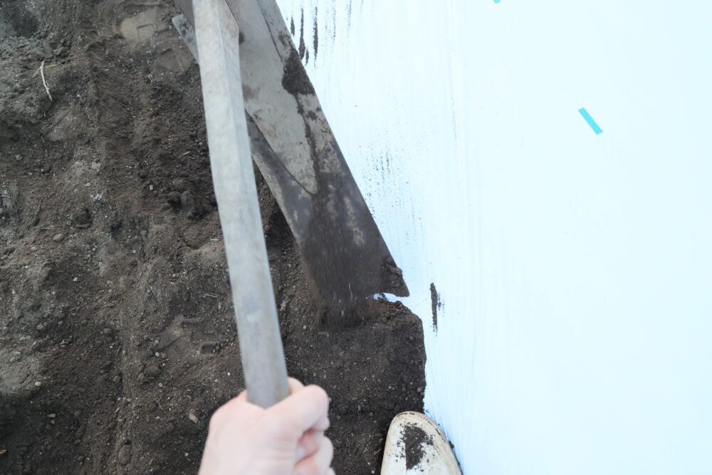 マルチの端に鍬ですくった土を乗せる